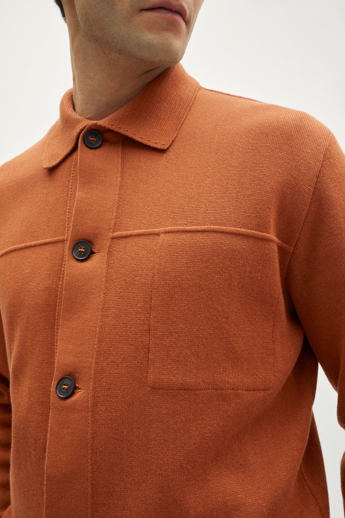 Close-up of a person wearing an orange shirt with button details on a white background