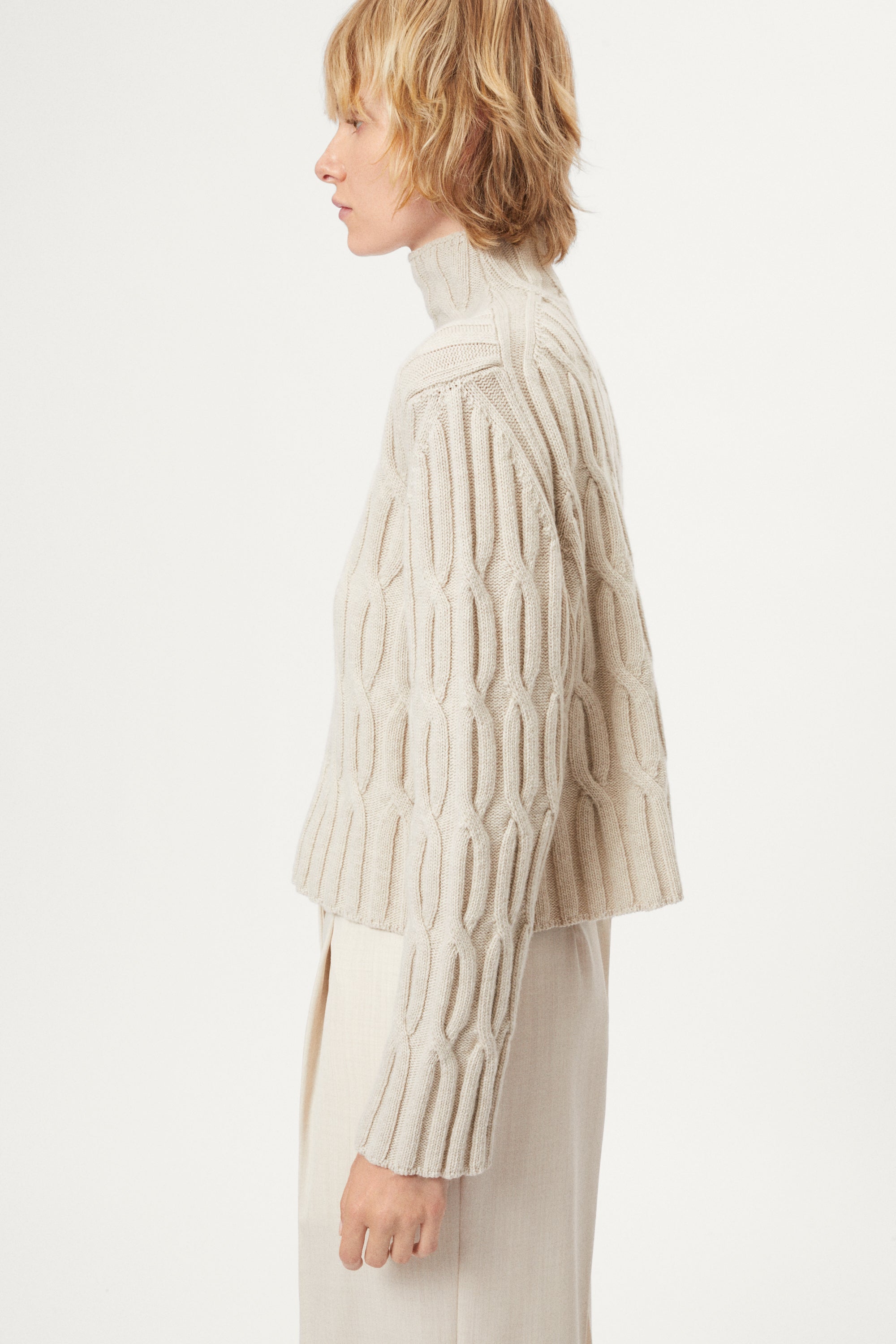woman wearing a woolen beige cable knit turtleneck sweater on a white background