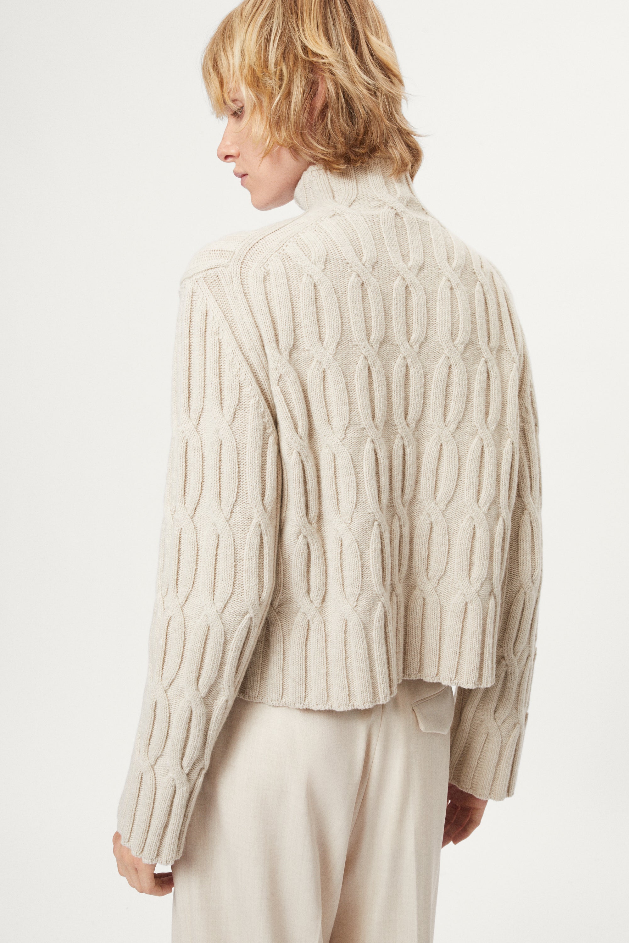woman wearing a woolen beige cable knit turtleneck sweater on a white background