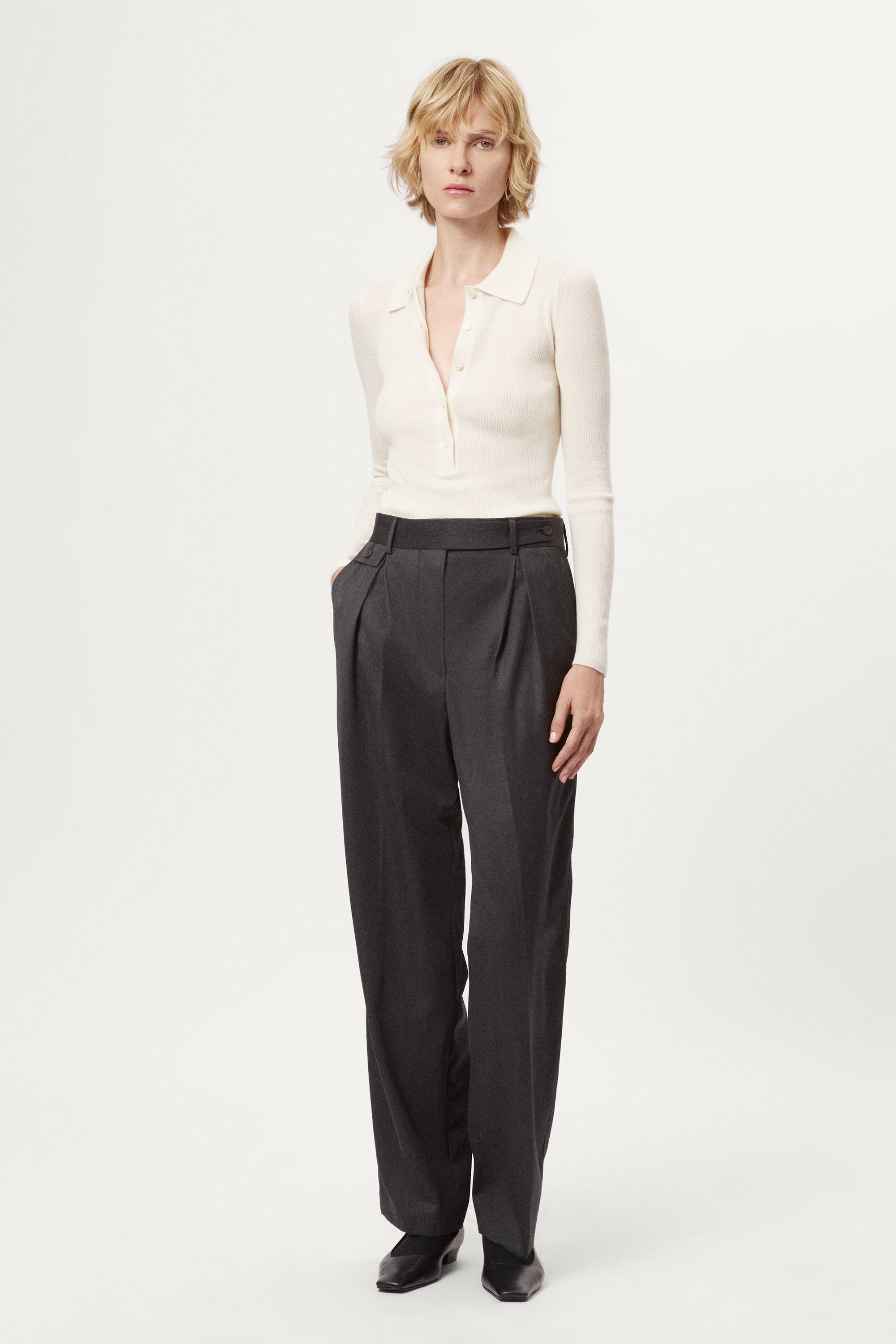 Woman wearing a white blouse and dark gray pants on a white background