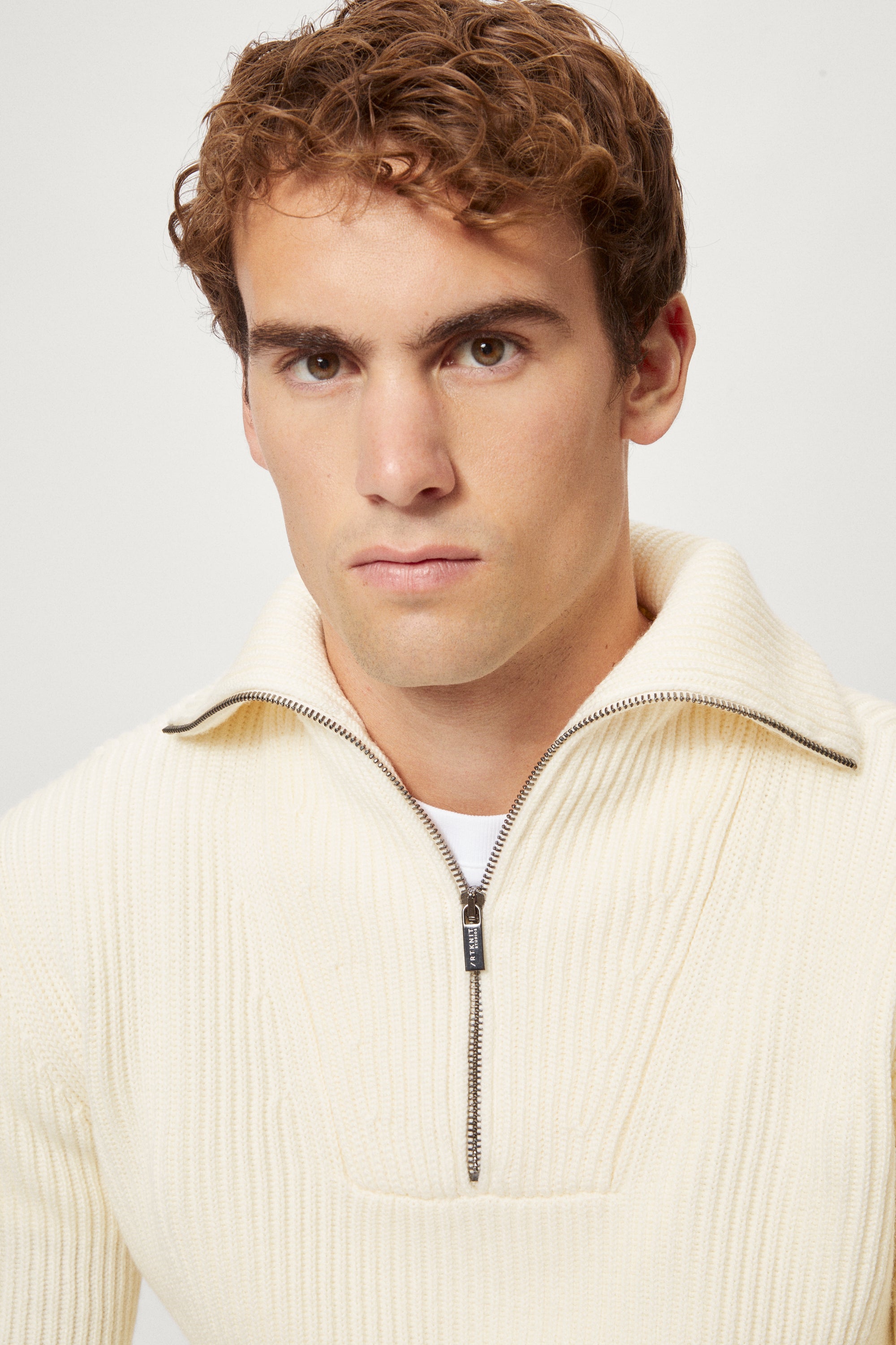 Man wearing a cream half-zip sweater against a white background