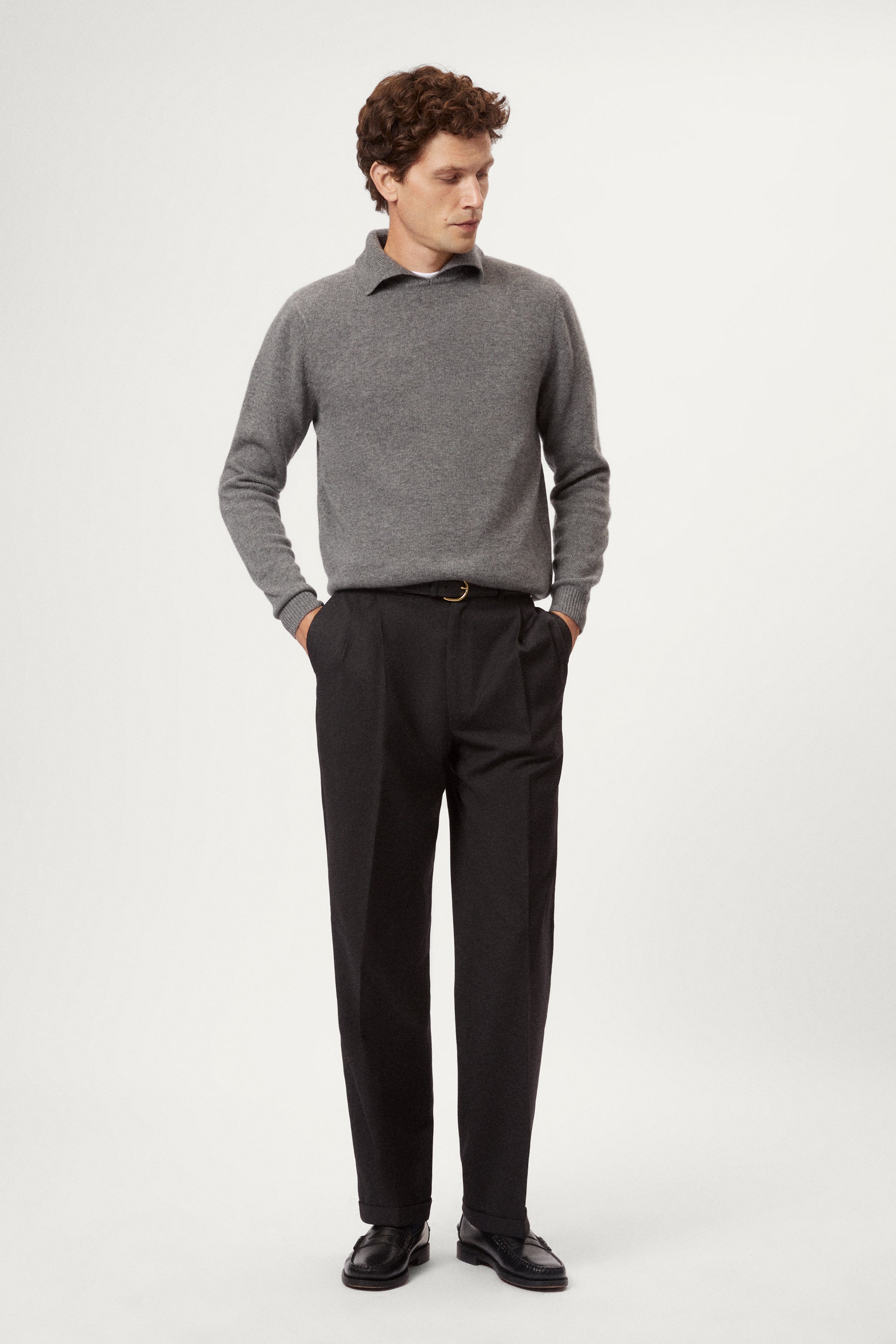 Man wearing a gray woolen polo sweater and black pants on a white background