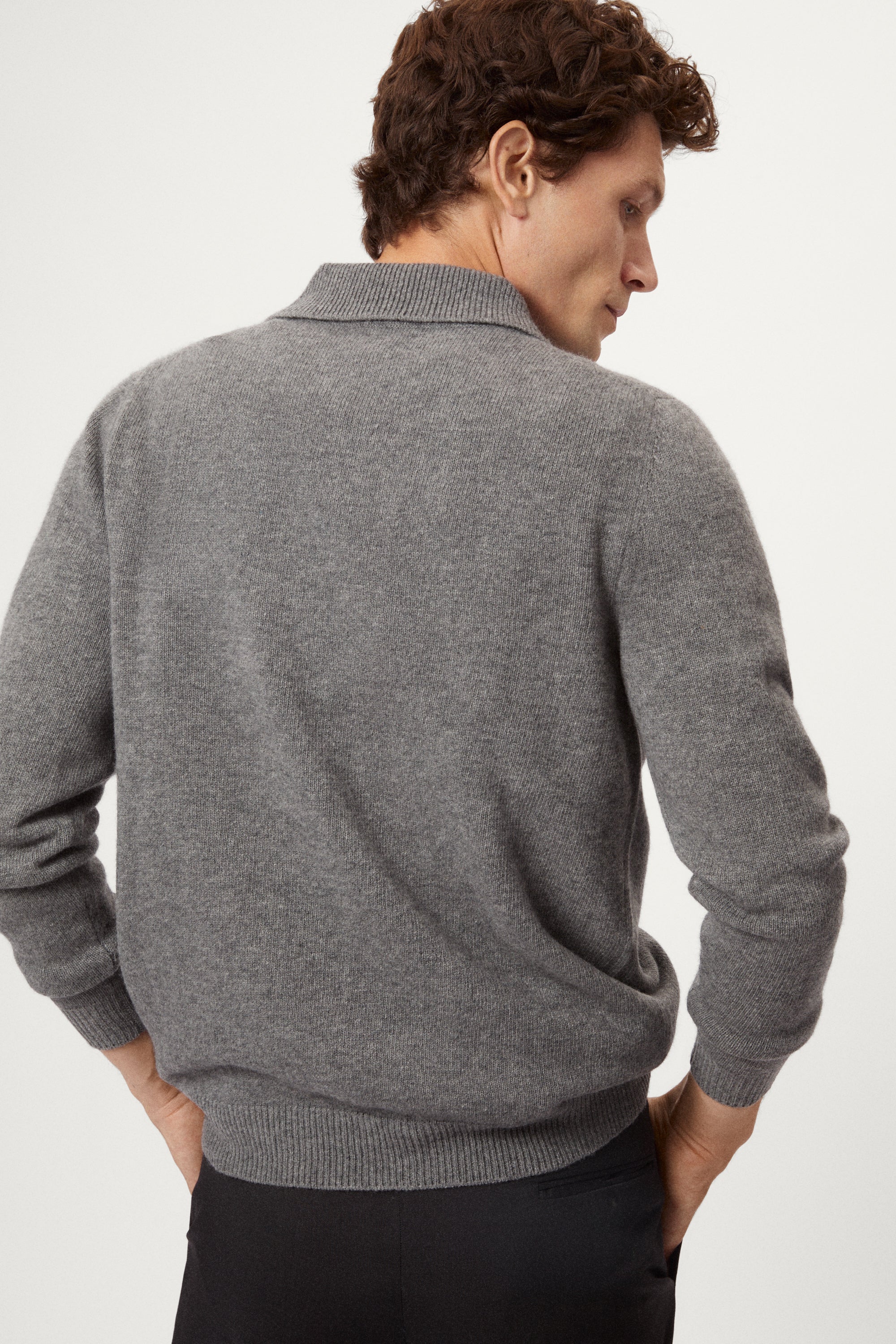 Man wearing a gray woolen polo sweater and black pants on a white background