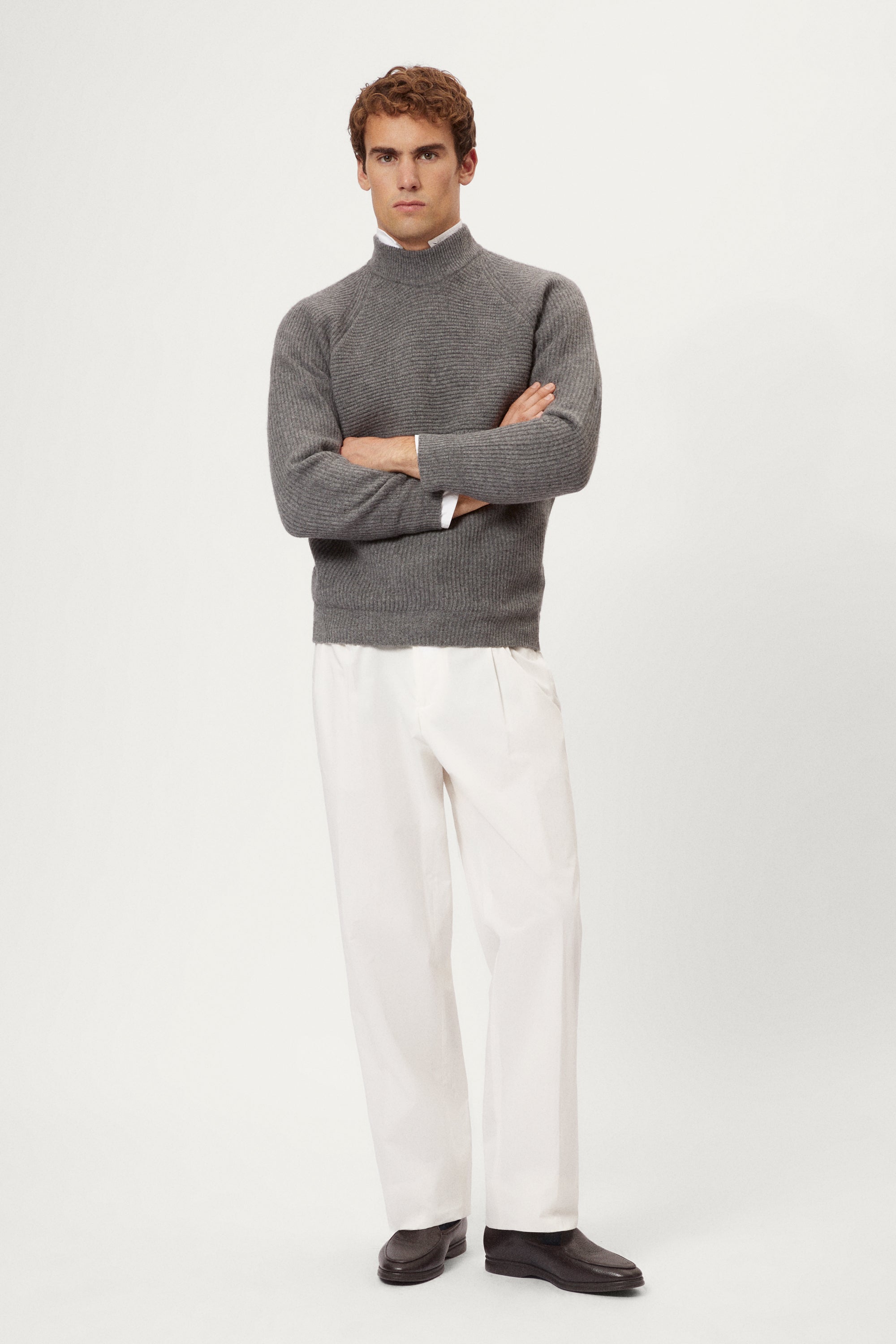 Man wearing a gray ribbed sweater and white pants on a light background