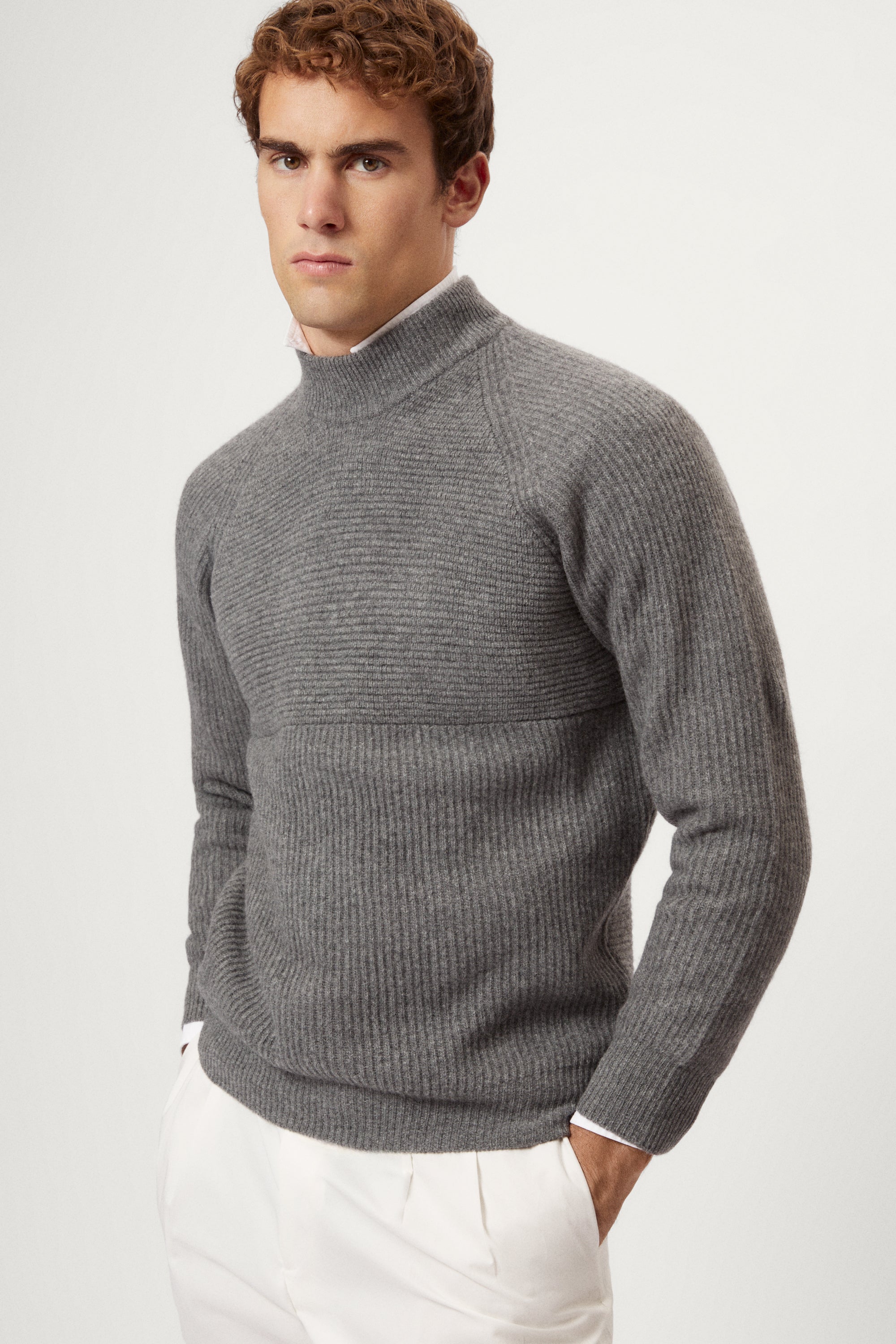 Man wearing a gray ribbed sweater and white pants on a light background