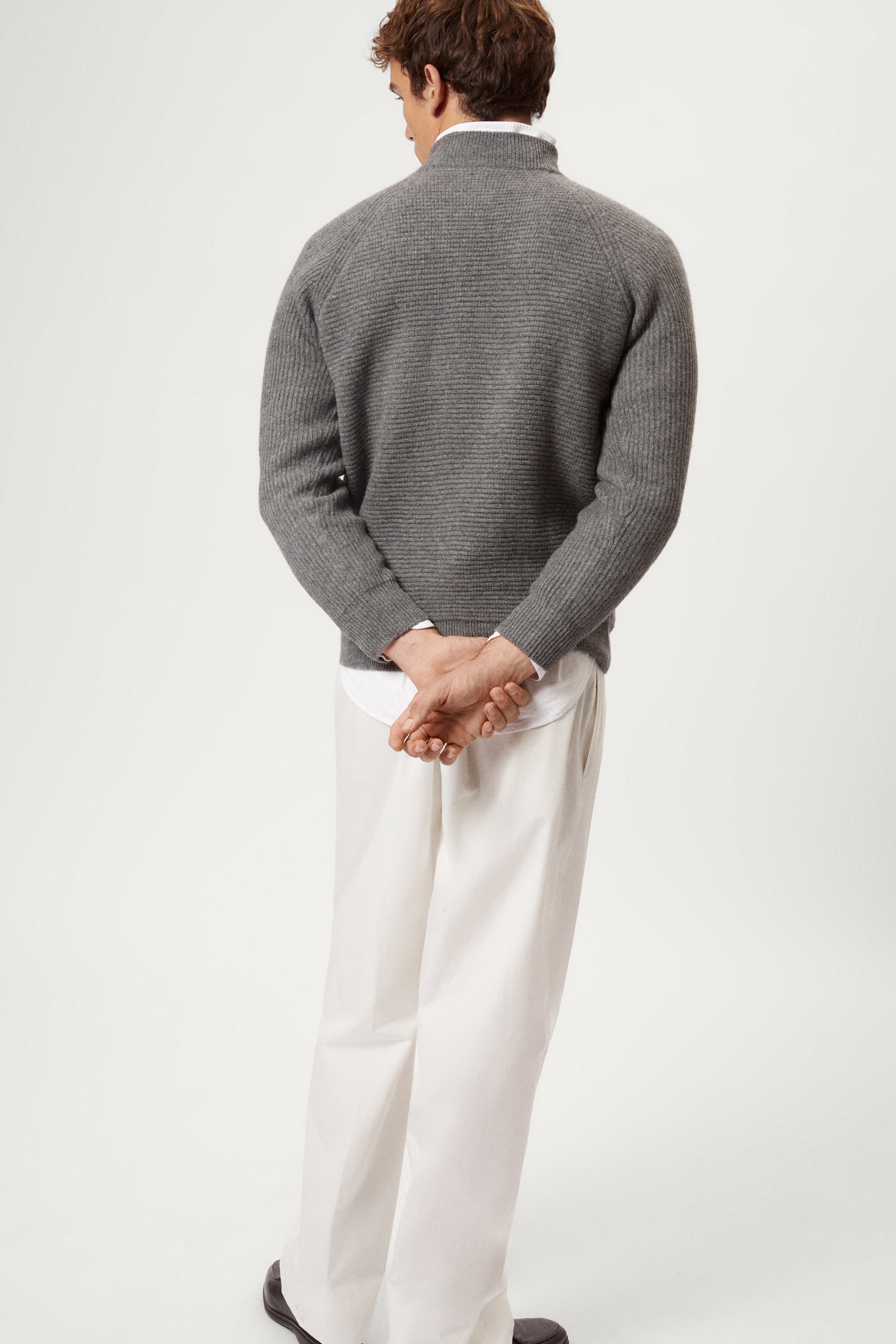 Man wearing a gray ribbed sweater and white pants on a light background