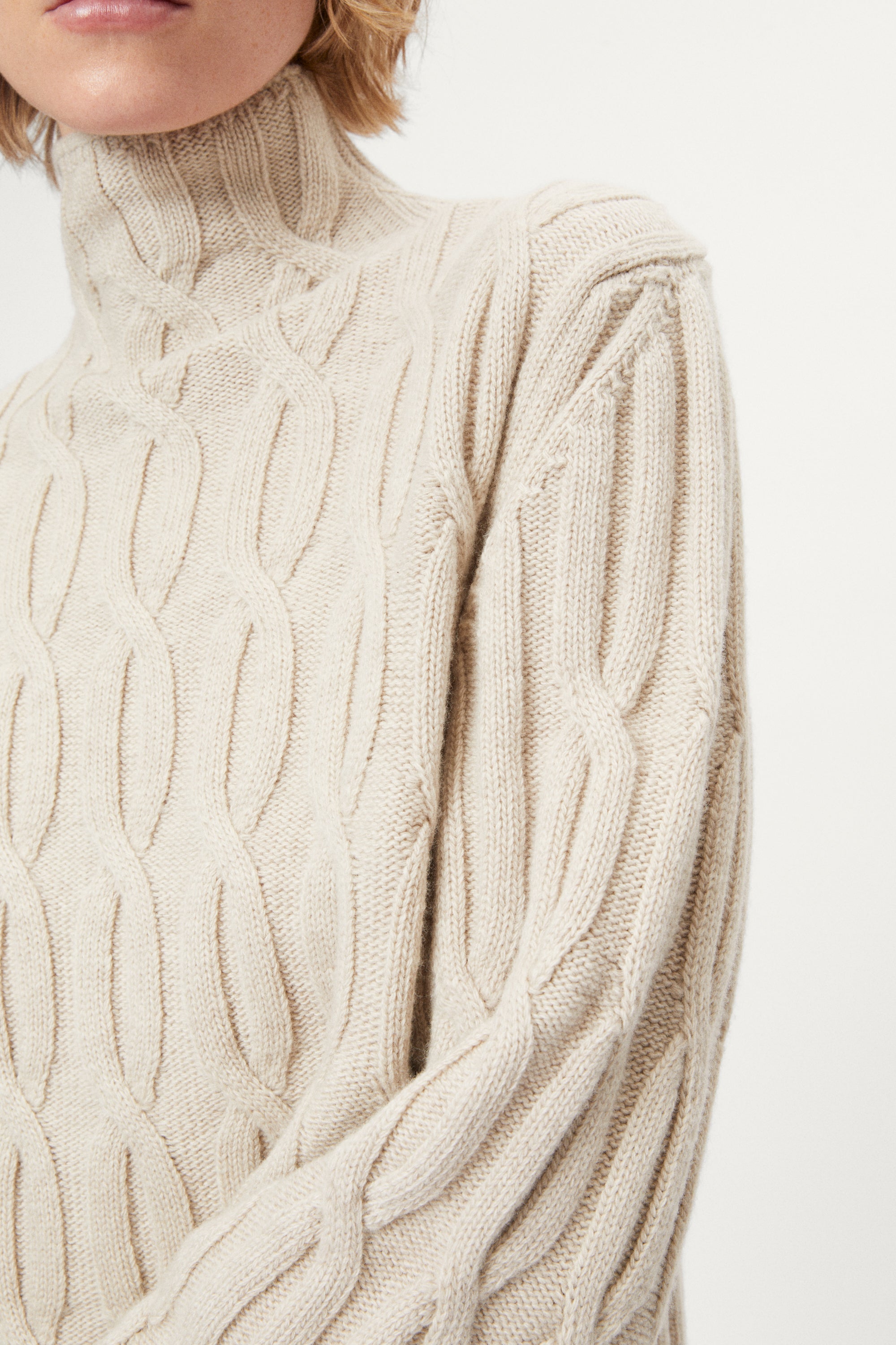 woman wearing a woolen  beige cable knit turtleneck sweater on a white background