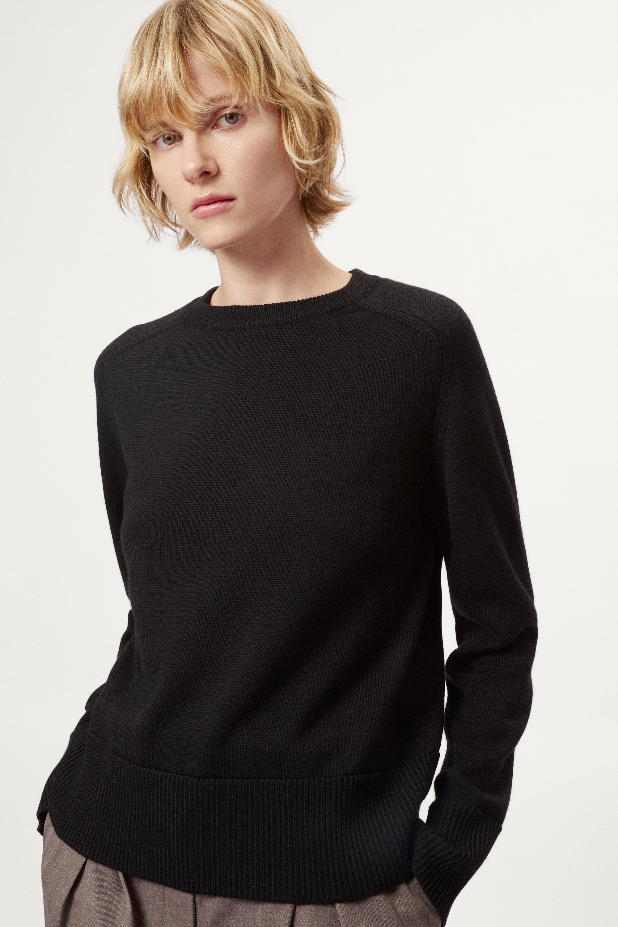 Woman wearing a black merino  sweater on a plain background