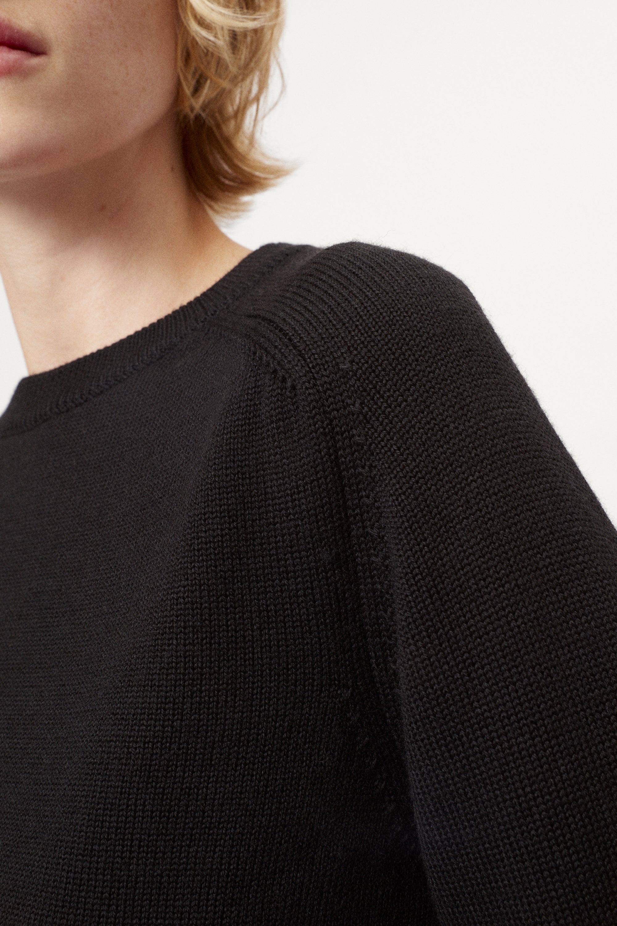 Woman wearing a black merino  sweater on a plain background