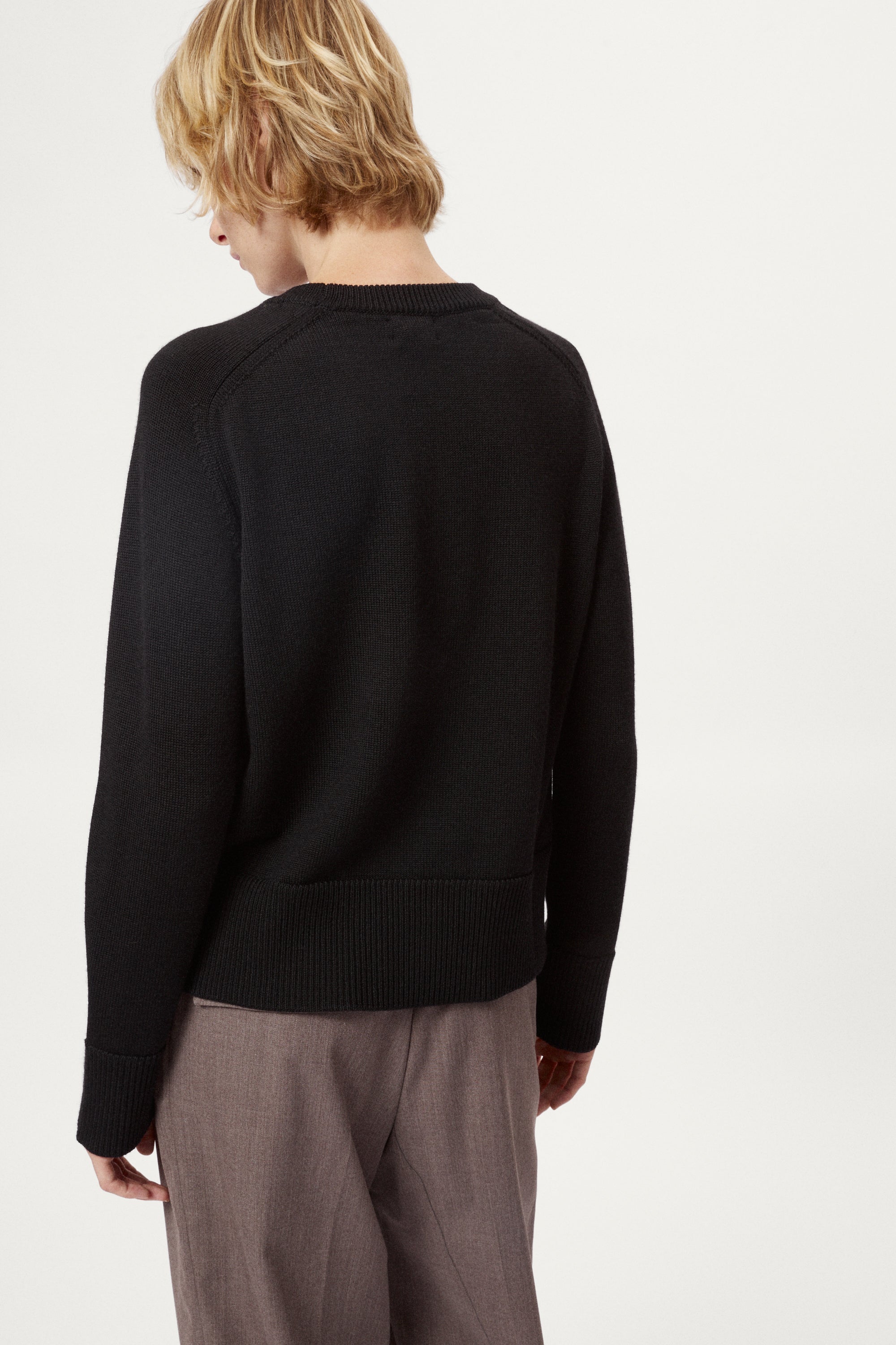 Woman wearing a black merino  sweater on a plain background