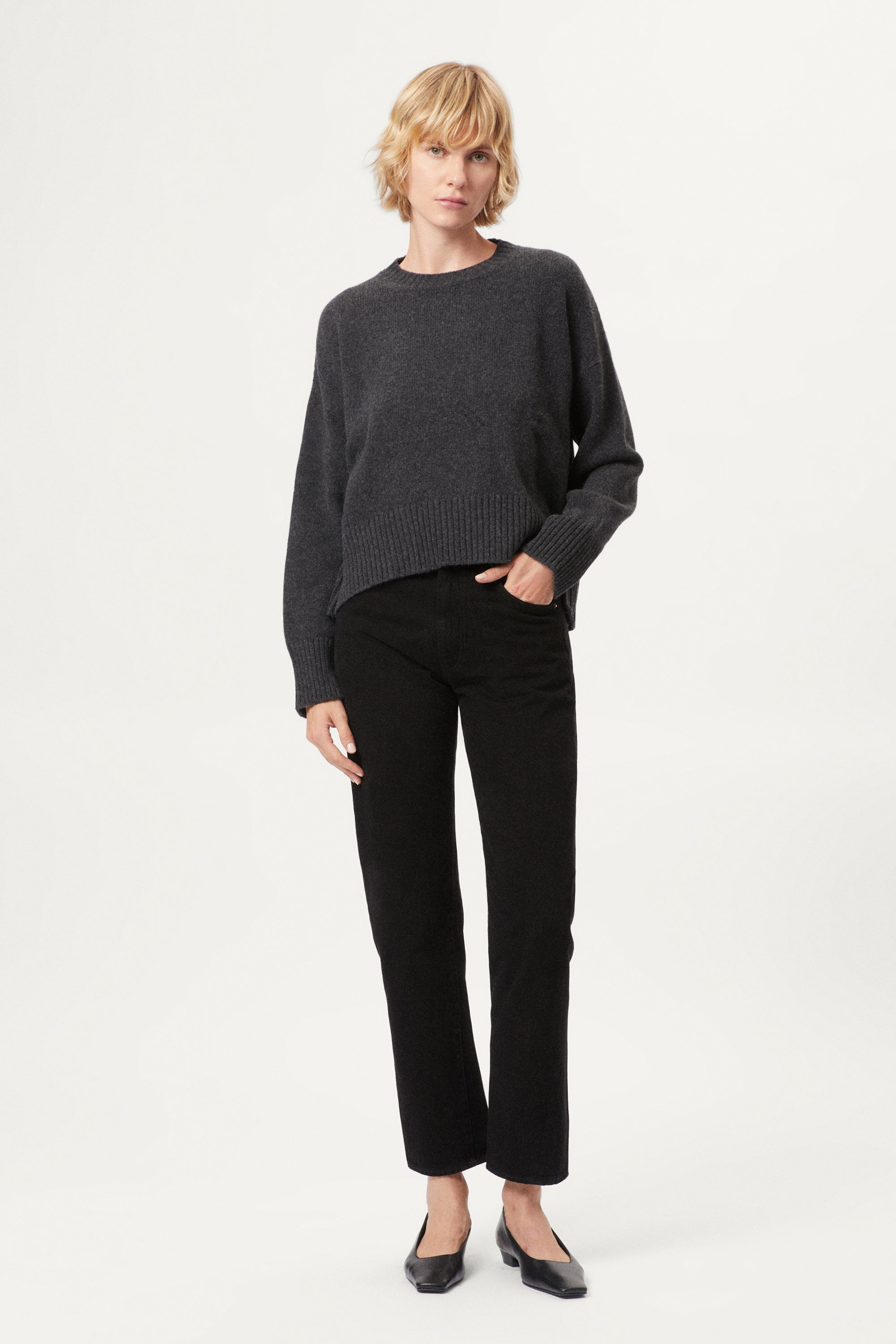 Woman wearing a woolen dark gray sweater and black pants on a white background