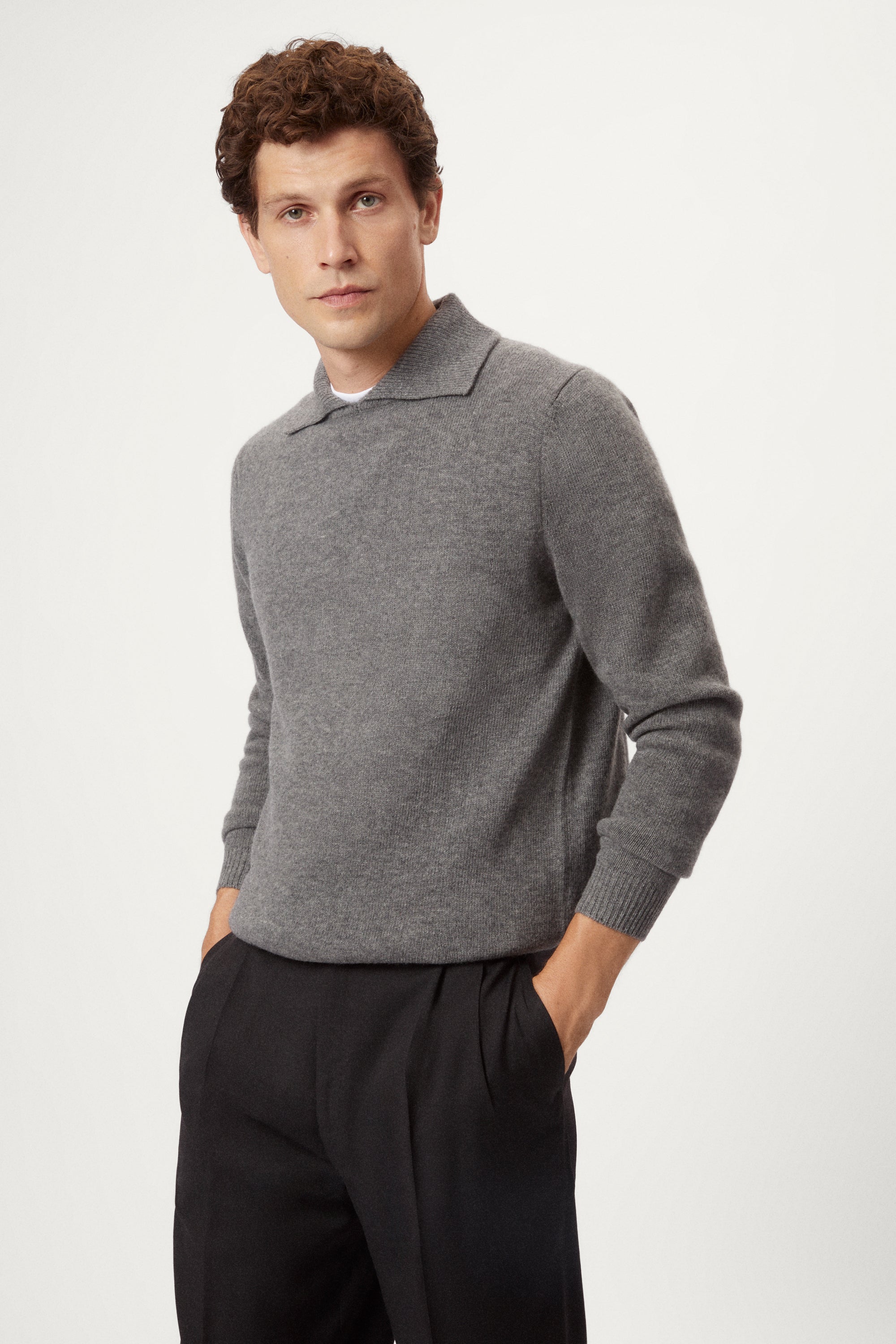 Man wearing a gray woolen  polo sweater and black pants on a white background