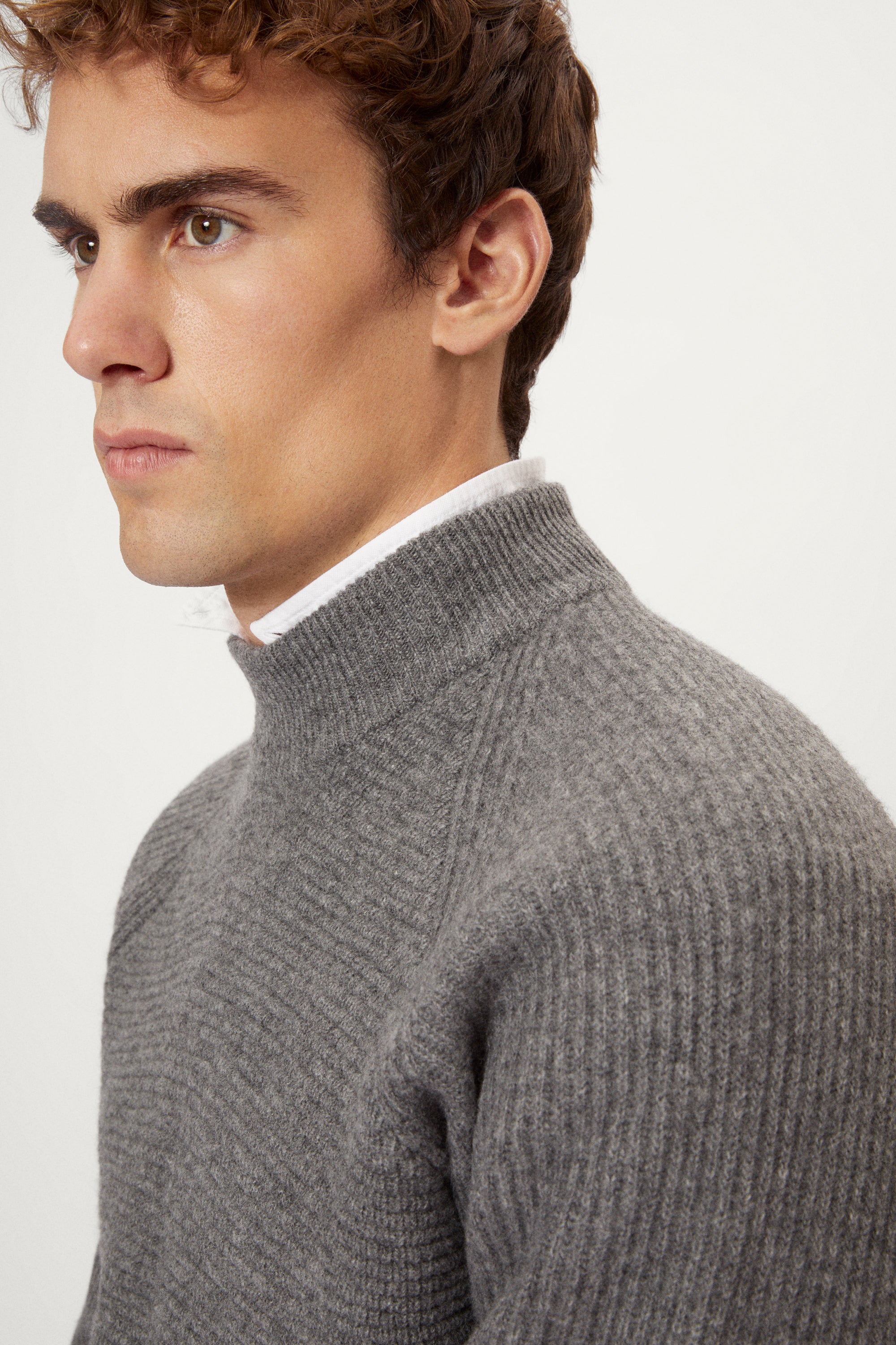 Man wearing a gray  ribbed sweater and white pants on a light background